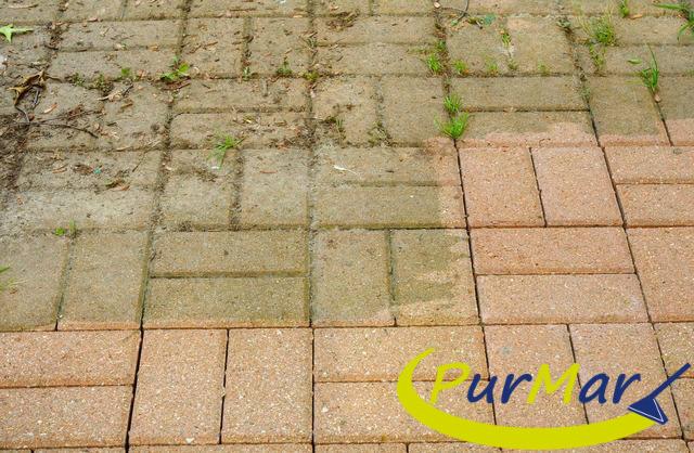 Częściowo wyczyszczona kostka brukowa, widoczna różnica między brudną, zielonkawą częścią a czystą, różową, z logo firmy w prawym dolnym rogu.