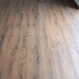 Nowo ułożona, brązowa podłoga z paneli laminowanych, imitujących drewno, widoczna z perspektywy podłogi, z fragmentem białej zabudowy w tle.