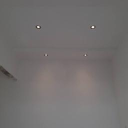 Remont-ownia - Białe wnętrze z czterema okrągłymi punktowymi lampami sufitowymi o ciepłej barwie światła, równomiernie rozmieszczonymi na gładkim suficie.