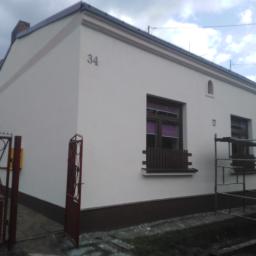 Remont-ownia - Odnowiona elewacja domu jednorodzinnego z numerem 34, widoczne rusztowanie przy ścianie bocznej, otwarte wejście na posesję.