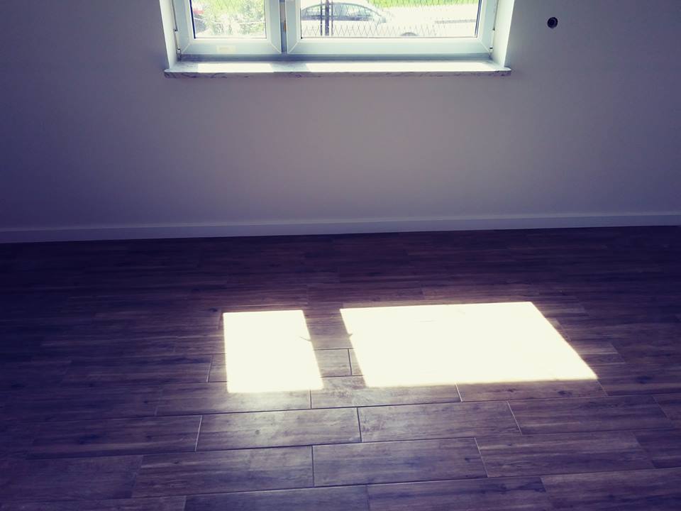 Ułożona podłoga z płytek imitujących drewno w pustym pokoju w Częstochowie, z oknem dachowym i plamami światła słonecznego.