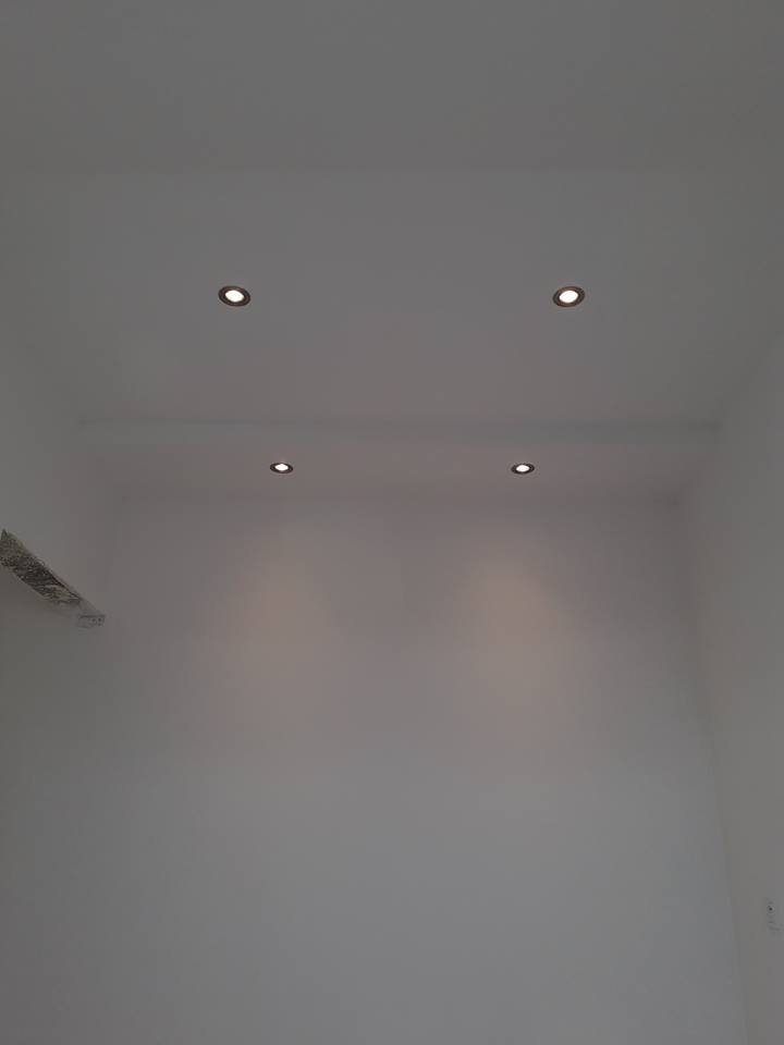 Białe wnętrze z czterema okrągłymi punktowymi lampami sufitowymi o ciepłej barwie światła, równomiernie rozmieszczonymi na gładkim suficie.