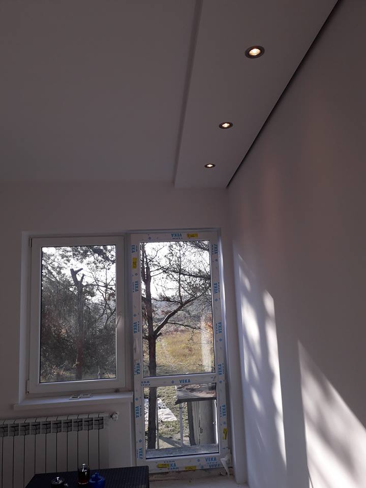 Wnętrze pokoju po remoncie z widokiem na okno, z zamontowanymi oknami PCV marki VEKA, z podwieszanym sufitem z oświetleniem punktowym.