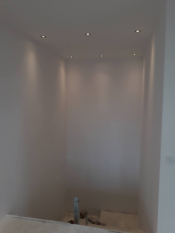 Wnęka z oświetleniem punktowym w suficie, ściany pomalowane na jasny kolor, widoczne ślady prac wykończeniowych na podłodze, drabina oparta o ścianę.