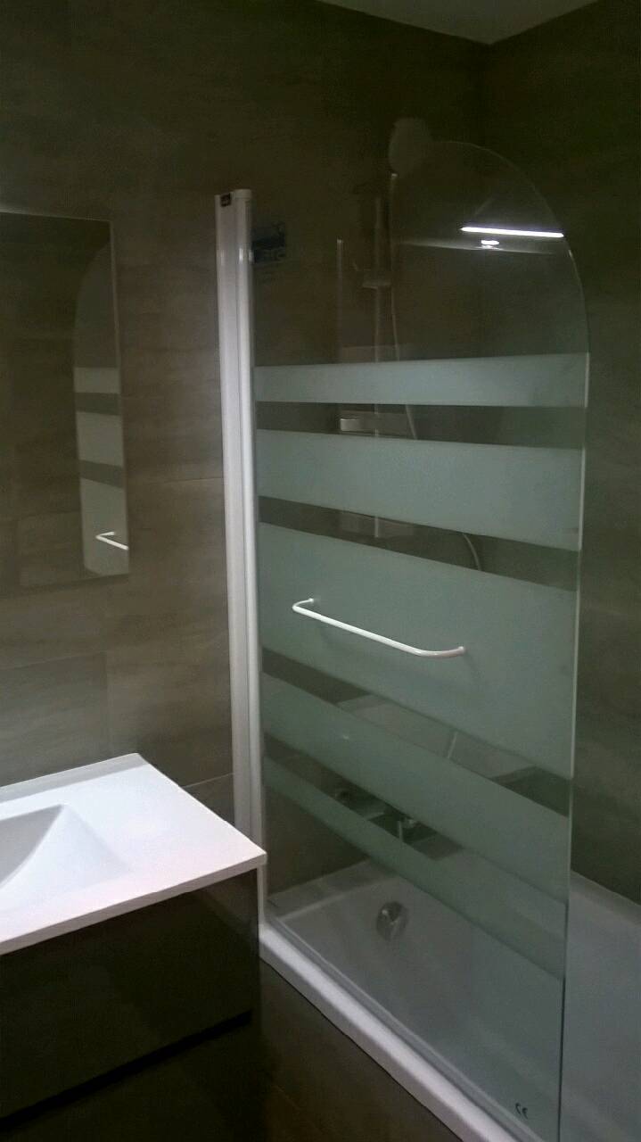 Nowoczesna kabina prysznicowa z matowymi pasami, umywalka z szafką w łazience wykończonej płytkami w odcieniach szarości.