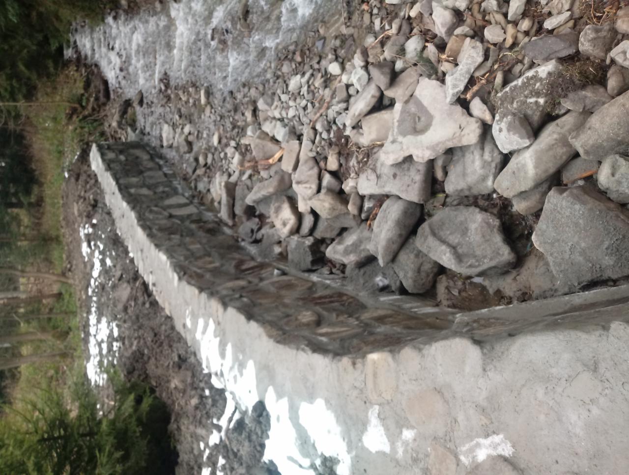 Umocnienie koryta rzeki wykonane z kamienia i betonu, widok z góry na fragment cieku wodnego i brzeg z roślinnością.