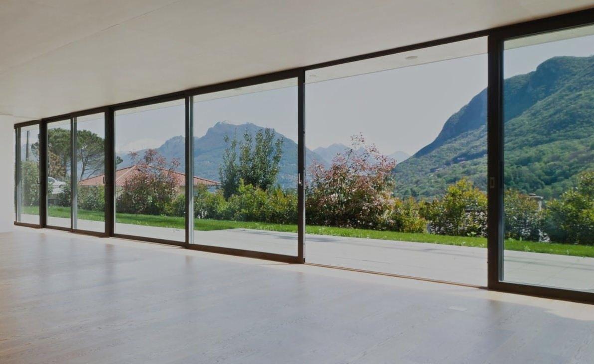 Wnętrze z panoramicznymi przesuwnymi oknami z widokiem na góry i ogród, jasna podłoga, nowoczesny design.