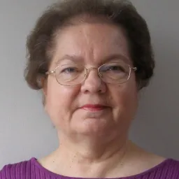 Portret kobiety w okularach i fioletowej bluzce na szarym tle.