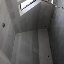 Hetman Bud - Wnętrze w trakcie prac wykończeniowych: ściany przygotowane pod malowanie, widoczne łączenia płyt gipsowo-kartonowych i fragment drabiny oparty o ścianę.