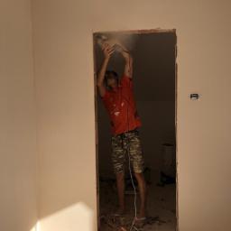 Hetman Bud - Pracownik w czerwonej koszulce poszerza otwór drzwiowy w ścianie, używając szlifierki kątowej, z widocznymi odłamkami materiału na podłodze.