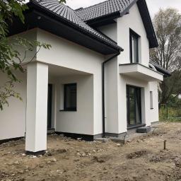 Hetman Bud - Nowoczesny dom jednorodzinny z białą elewacją i czarnym dachem, widok z boku na niezagospodarowany teren.