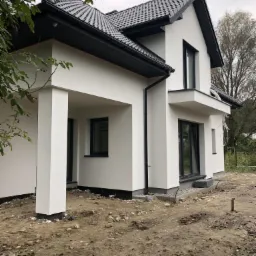 Nowoczesny dom jednorodzinny z białą elewacją i czarnym dachem, widok z boku na niezagospodarowany teren.