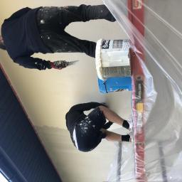 Hetman Bud - Dwóch pracowników wykończeniowych szpachluje sufit na budowie, widoczne wiadro z masą szpachlową, poziomica i folia ochronna.