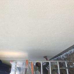 Hetman Bud - Dwóch pracowników na drabinie szpachluje sufit wewnątrz budynku, widoczne nierówności na ścianie w tle.