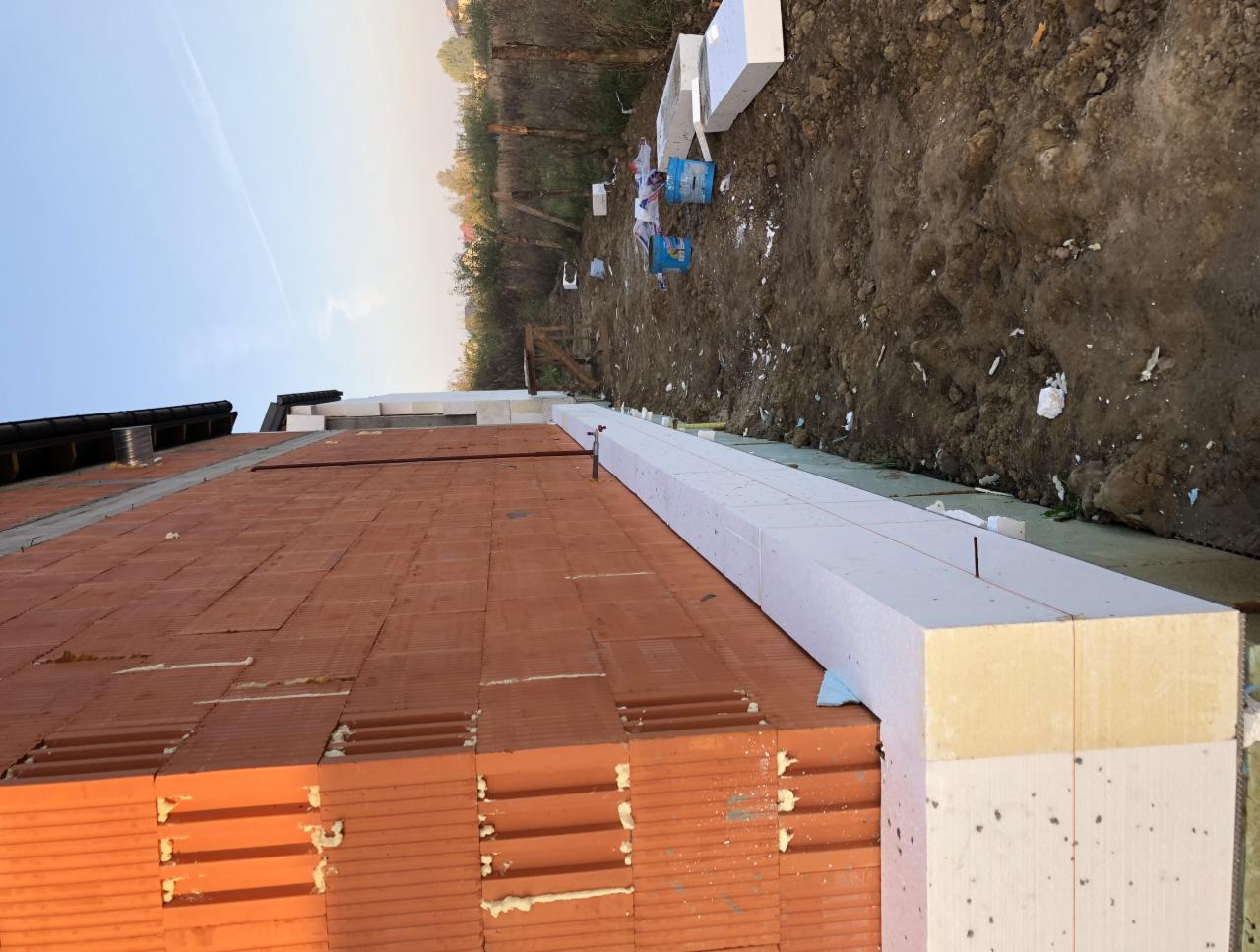 Widok z góry na budynek w trakcie ocieplania elewacji, widoczne bloczki z czerwonej cegły, białe płyty izolacyjne i fragment dachu.