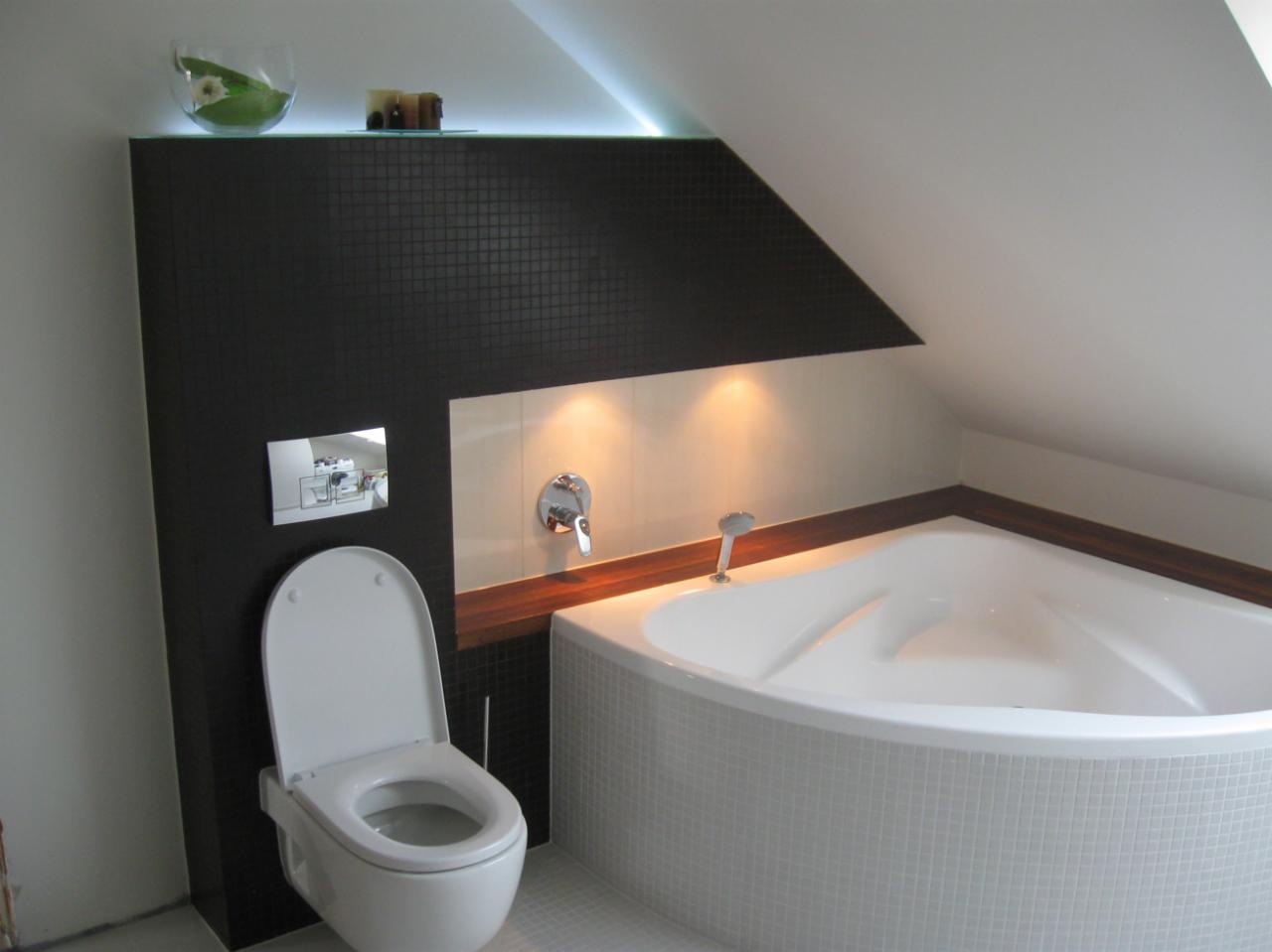 Nowoczesna łazienka na poddaszu z czarną mozaiką, podświetlaną półką i narożną wanną obłożoną białą mozaiką oraz wiszącą toaletą z chromowanym przyciskiem.