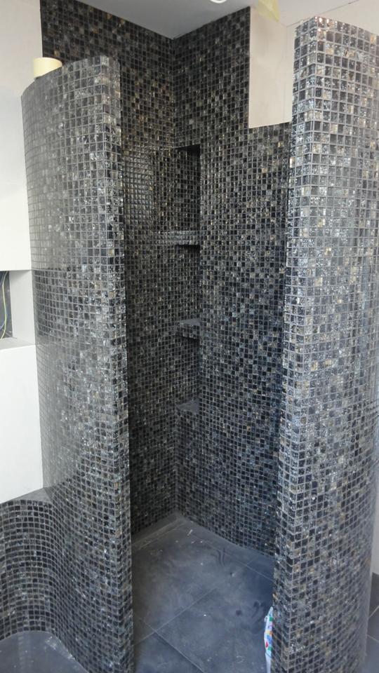 Wykończona kabina prysznicowa z czarnej mozaiki kwadratowej z półkami wnękowymi, widoczne niedociągnięcia w postaci resztek kleju i niezabezpieczonych krawędzi.