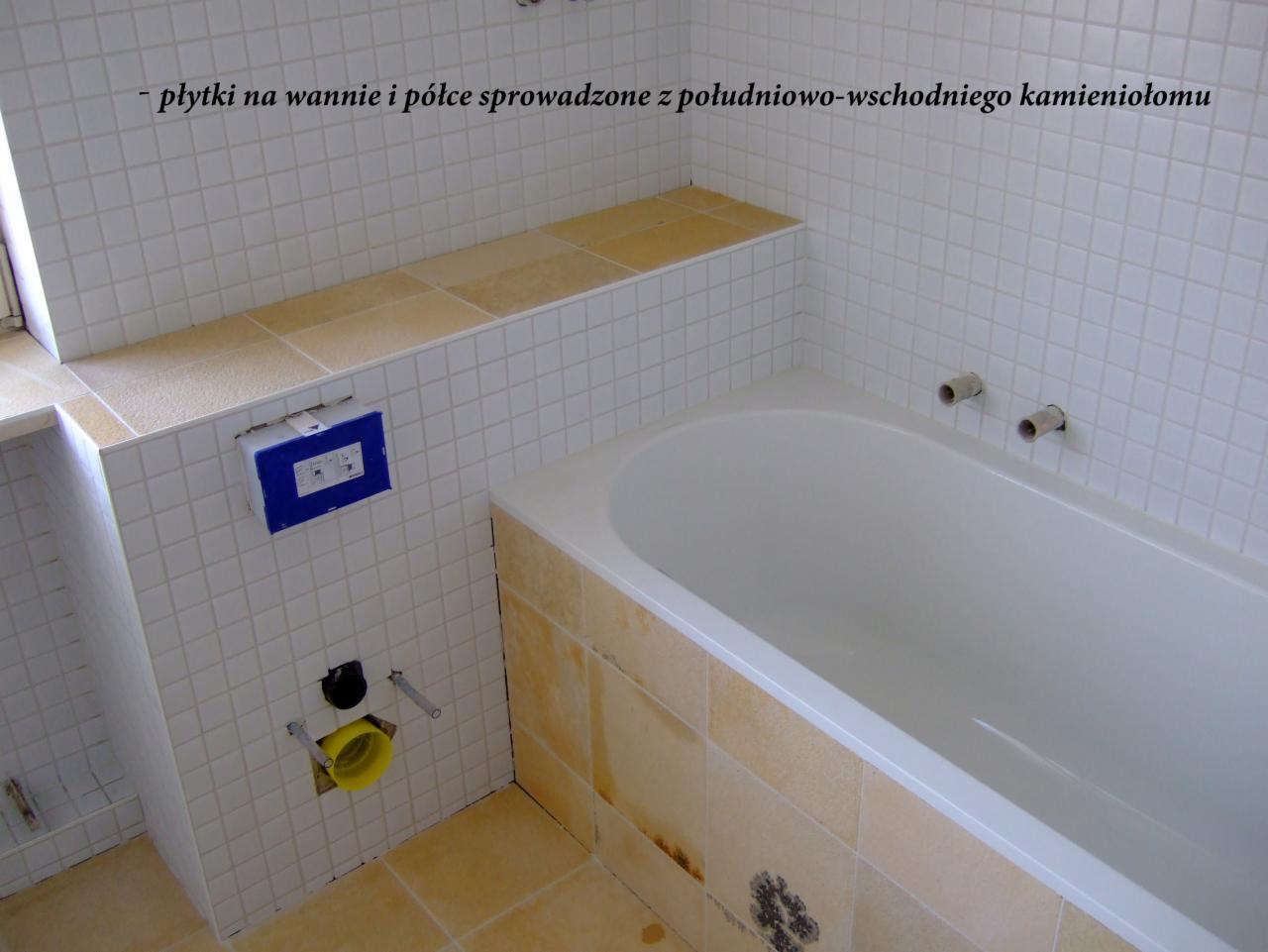 Wykończona łazienka z wanną, obłożona białymi płytkami z beżowymi akcentami na półce i obudowie wanny, widoczne rury i instalacja podtynkowa.