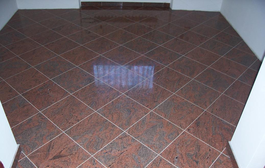 Połyskująca, ciemnoczerwona podłoga z płytek ułożonych w karo, z jasnymi fugami i odbiciem okna.