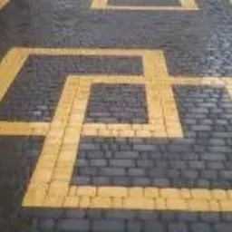 Ułożona nawierzchnia z ciemnoszarej kostki z żółtym wzorem geometrycznym w kształcie połączonych kwadratów, widok z góry, lekko z boku.