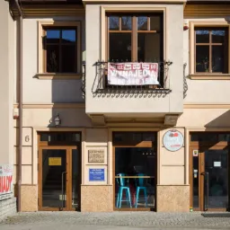 Fasada kamienicy z lokalami użytkowymi na parterze, baner z napisem 'Lokale do wynajęcia' na balkonie, szyld 'Kancelaria Radcy Prawnego' obok wejścia.