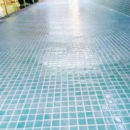 Świeżo położona, błyszcząca mozaika w odcieniach błękitu i zieleni na ścianie i podłodze, z widocznymi fugami, tworząca geometryczny wzór w łazience w trakcie remontu.