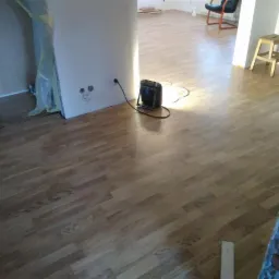 Parkiet ułożony w jodełkę, suszony nagrzewnicą elektryczną w trakcie remontu, widoczne przygotowane ściany i fragment odsłoniętej cegły.