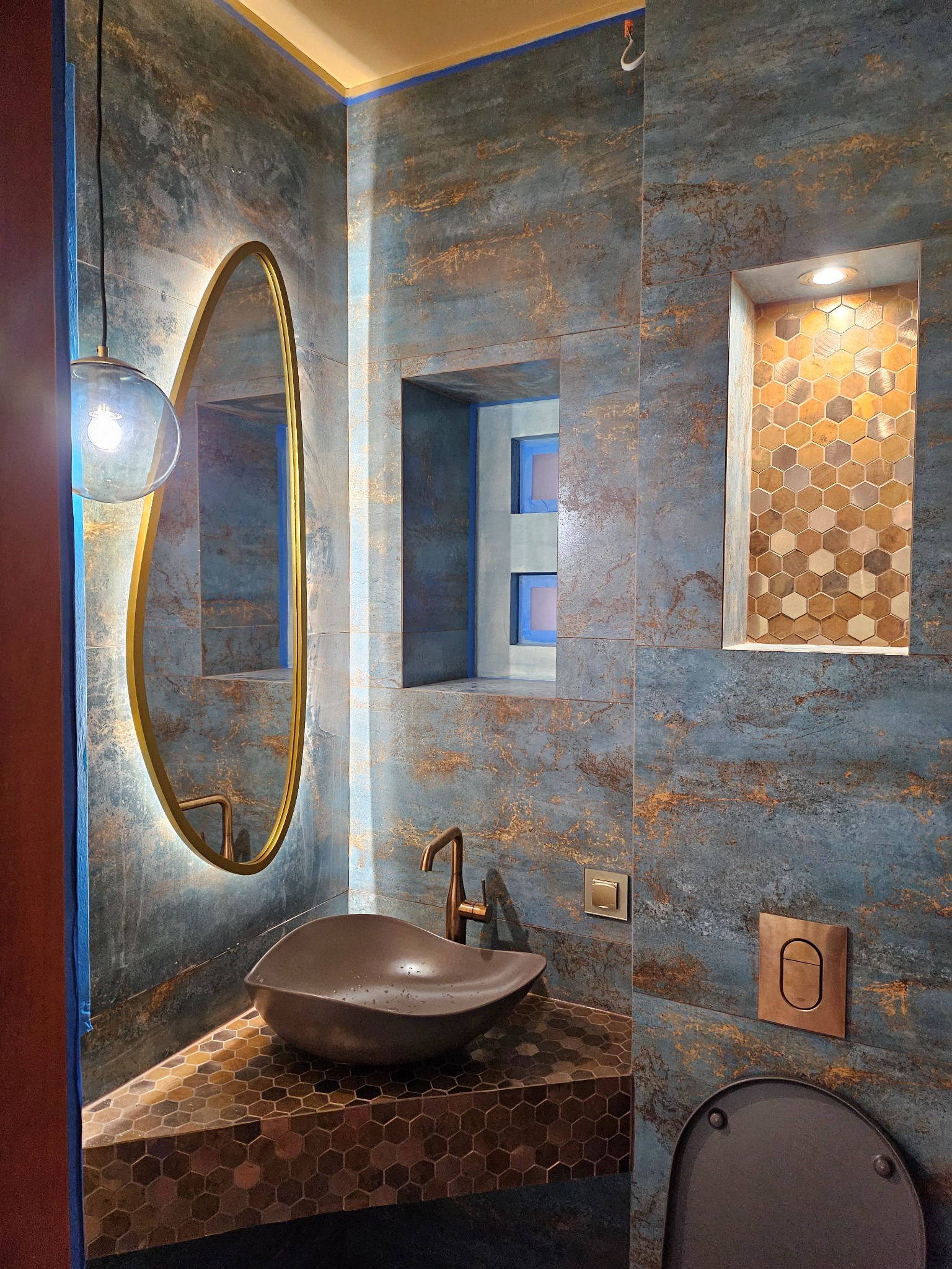 Nowoczesna łazienka z umywalką w kształcie misy, lustrem z podświetleniem LED, płytkami imitującymi rdzę i mozaiką heksagonalną w niszy.