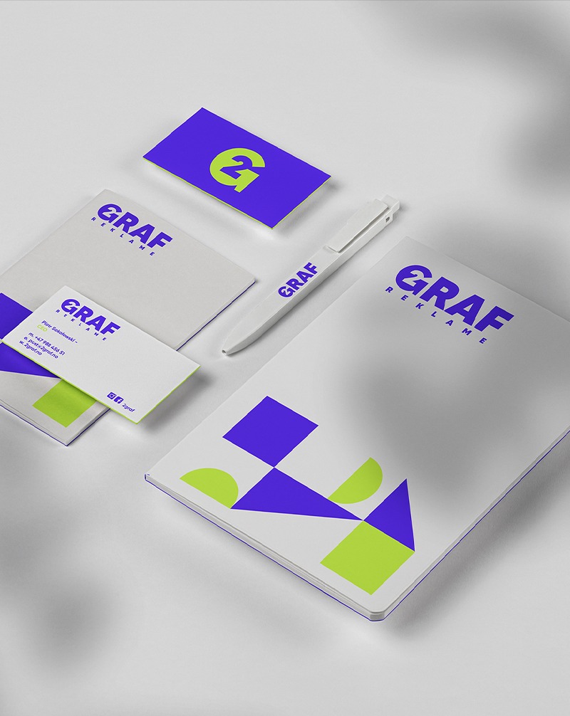 Zestaw identyfikacji wizualnej: wizytówki, notesy i długopis z logo 'Graf Reklame' w kolorach fioletu i limonki, na białym tle, w minimalistycznym stylu.