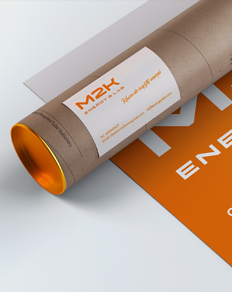 Tubka z logo M2K Energy & Lab, etykieta z danymi kontaktowymi, pomarańczowy plakat z fragmentem nazwy firmy. Prezentacja identyfikacji wizualnej.