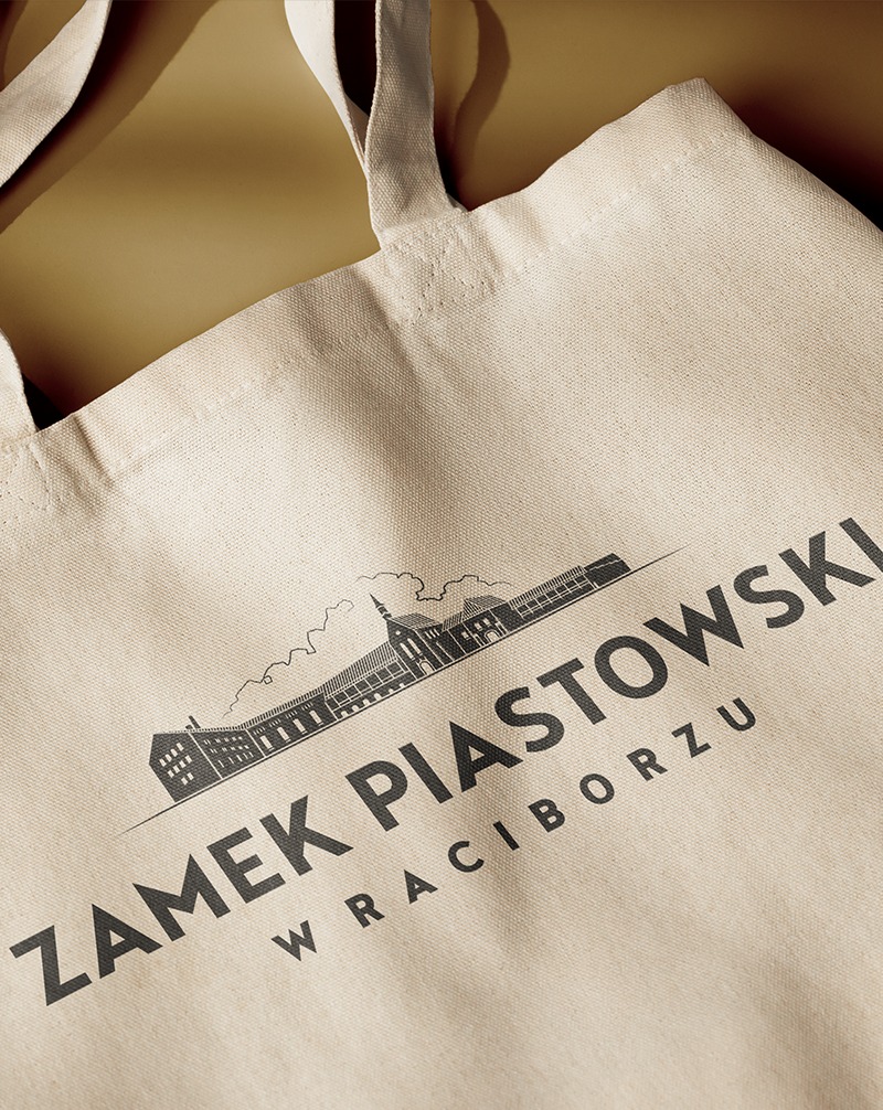Beżowa torba bawełniana z czarnym nadrukiem Zamku Piastowskiego w Raciborzu, widoczna z bliska pod kątem, z delikatnym cieniem na beżowym tle.