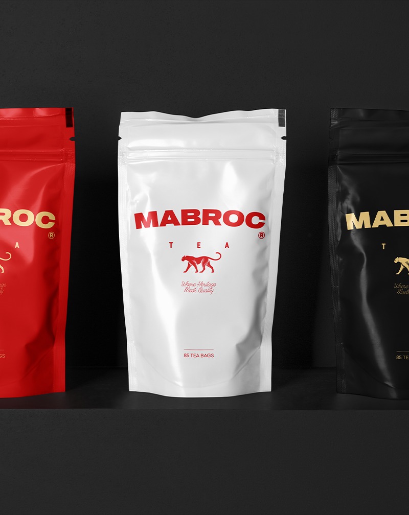 Trzy opakowania herbaty MABROC w różnych kolorach (czerwony, biały, czarny) na ciemnym tle. Elegancki branding herbaty z Raciborza.