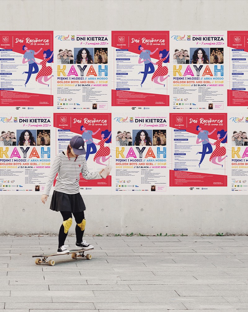 Plakat z Kayah na ścianie, obok osoba na deskorolce. Promocja wydarzenia muzycznego z artystką Kayah, w tle betonowa ściana z powielonym plakatem.