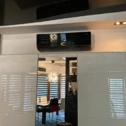 Czarny klimatyzator ścienny zamontowany nad szafką z lustrzanymi drzwiami w nowoczesnym wnętrzu mieszkania.