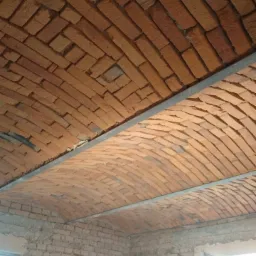 Ceglany łukowy sufit w trakcie budowy, widoczne metalowe profile, cegły ułożone w jodełkę, surowe ściany z cegły, drabina w rogu pomieszczenia.