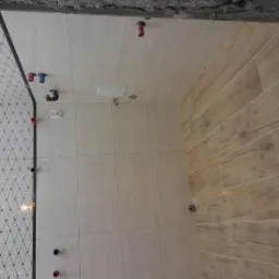 Ściany łazienki w trakcie remontu, widoczne płytki ceramiczne w dwóch wzorach: jasne kwadratowe i drewnopodobne prostokątne, instalacja wodna w ścianie, siatka wzmacniająca narożnik.