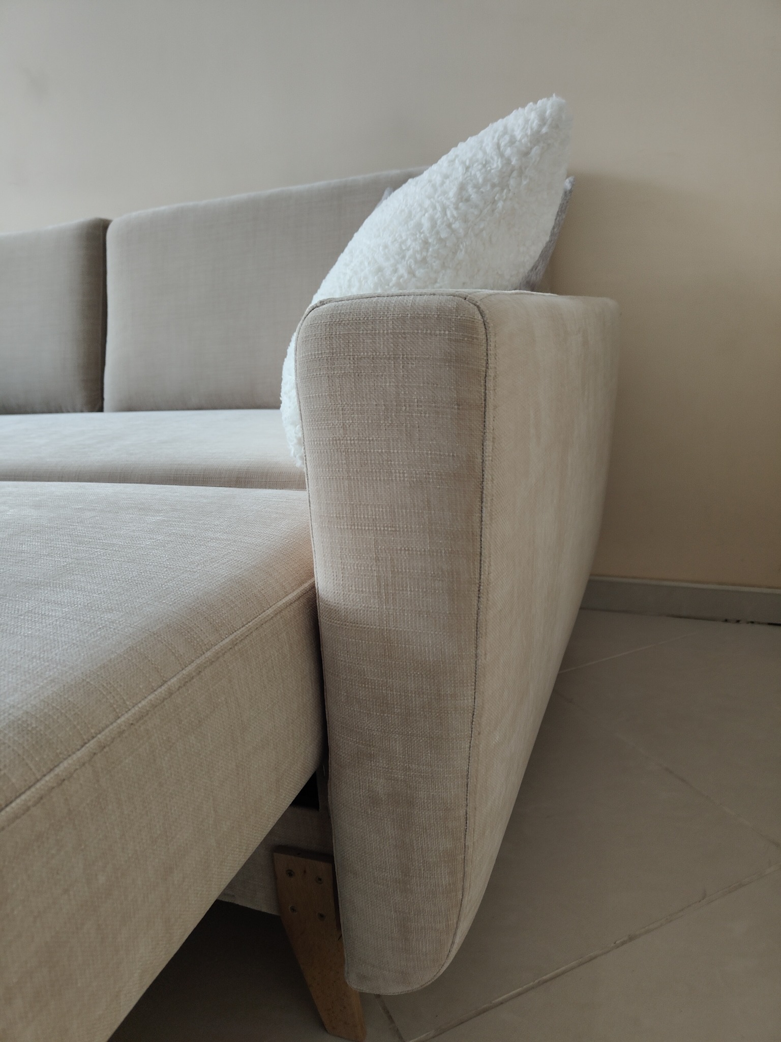 Beżowa sofa z poduszką w salonie, widok z boku, ukazujący detale tapicerki i solidną konstrukcję. Minimalistyczny design, jasne wnętrze.