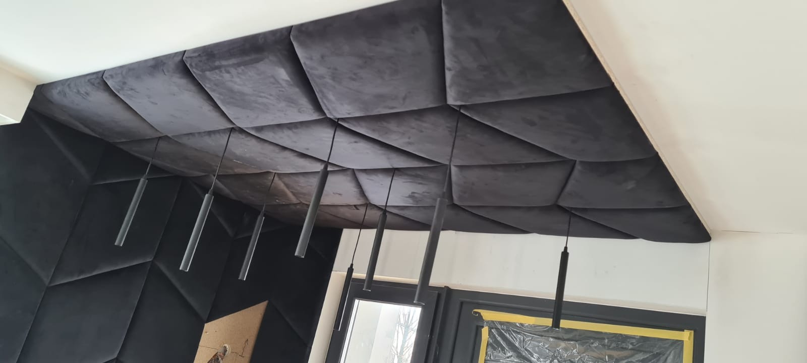 Tapicerowana ściana i sufit w geometryczne wzory, w odcieniach szarości, z wiszącymi lampami. Nowoczesny design wnętrza, realizacja na zamówienie.