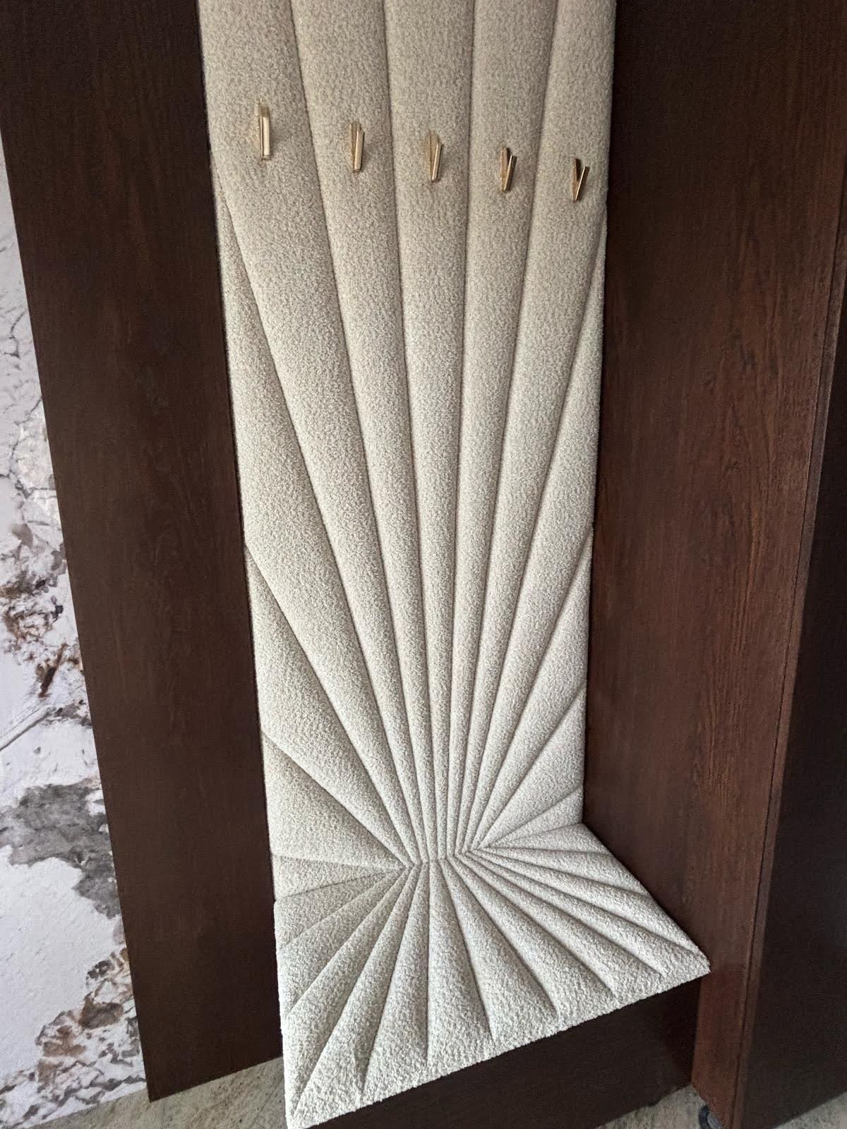 Tapicerowana ściana akustyczna w geometryczny wzór z wieszakami, zamontowana między ciemnymi panelami. Kremowa tkanina o wyraźnej fakturze. Unikalny projekt.