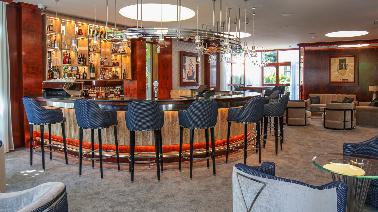 Elegancki bar w restauracji: wysokie, tapicerowane krzesła barowe z ciemnoniebieską tkaniną w kropki, drewniany bar z oświetleniem i butelkami alkoholi w tle.