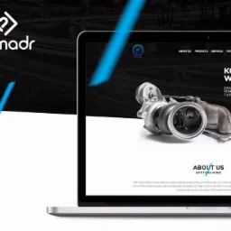 Laptop wyświetla stronę internetową firmy Kott Turbo Works z turbosprężarką na pierwszym planie, logo firmy akamadr widoczne w lewym górnym rogu.