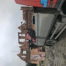 Czerwona ciężarówka z dźwigiem dostarcza cegły na plac budowy domu w trakcie wznoszenia murów, widoczne szare niebo.