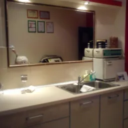 Wnętrze gabinetu z umywalką, sprzętem kosmetycznym i lustrem, w którym odbijają się certyfikaty na ścianie.