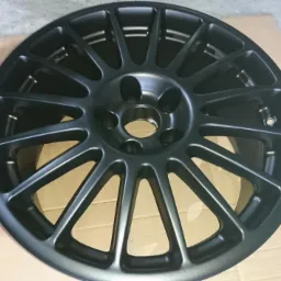 Matowa, grafitowa felga aluminiowa po malowaniu proszkowym, leżąca na kartonie, widok z przodu.