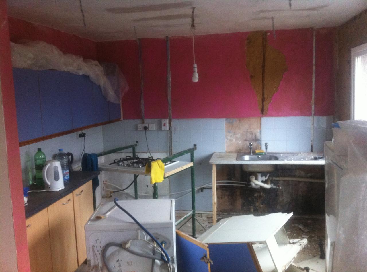 Kuchnia w Radziszowie w trakcie demontażu, widoczne różowe ściany, częściowo zerwane płytki, prowizoryczne podpory pod kuchenką gazową oraz zdemontowane szafki.