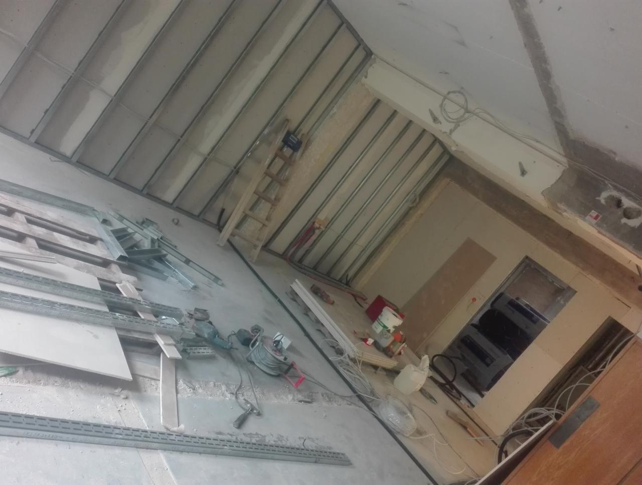 Montaż sufitu podwieszanego z metalowych profili i płyt gipsowo-kartonowych w trakcie realizacji, widoczne narzędzia i materiały budowlane na podłodze.