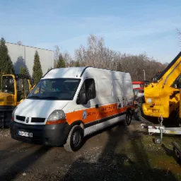 Biały van z pomarańczowym pasem i logo firmy na tle sprzętu budowlanego, w tym żółtej koparki i podnośnika koszowego. Na vanie widoczny numer telefonu i adres strony internetowej.