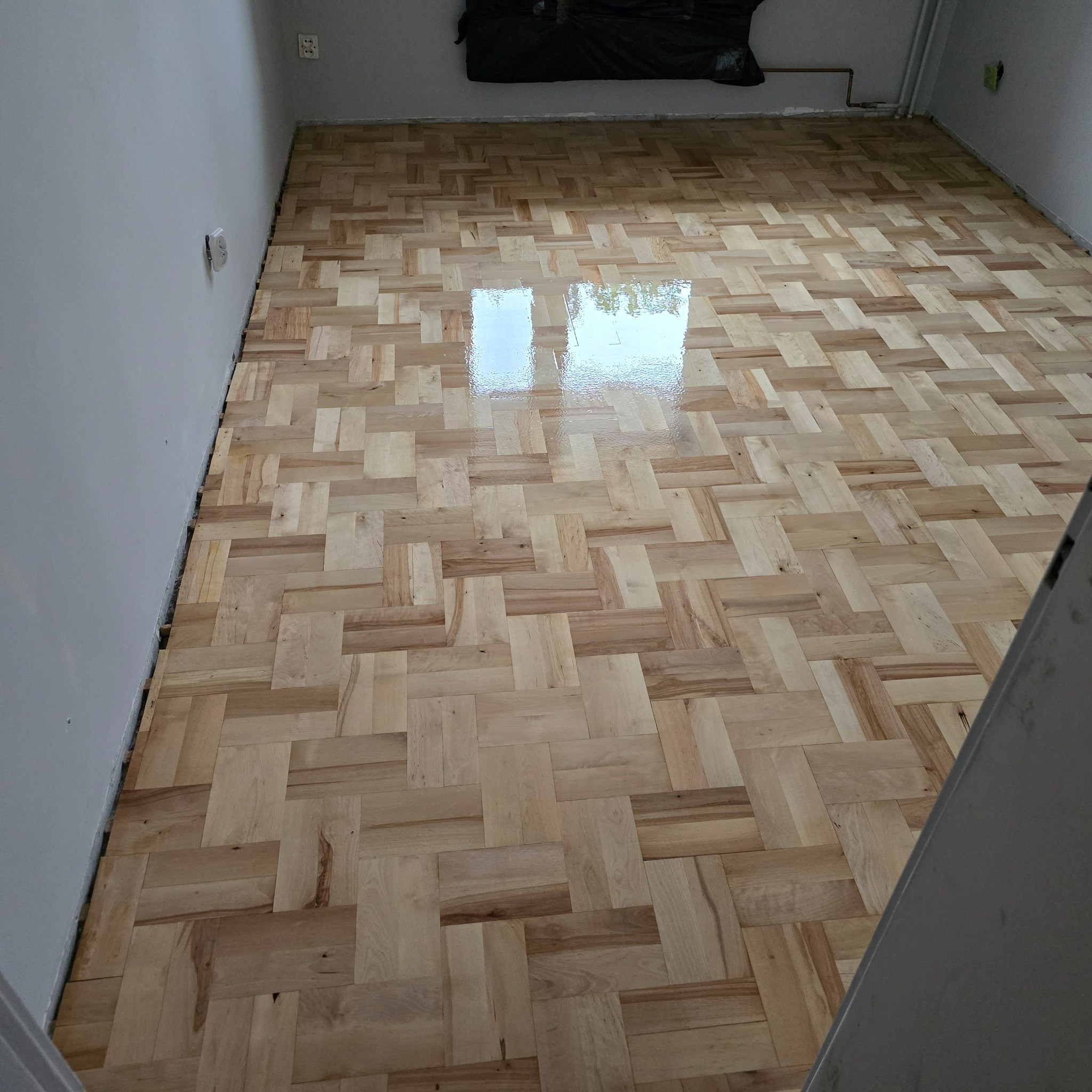 Świeżo polakierowana parkietowa podłoga ułożona w jodełkę, z widocznym odbiciem światła w lakierze, w trakcie remontu pomieszczenia.