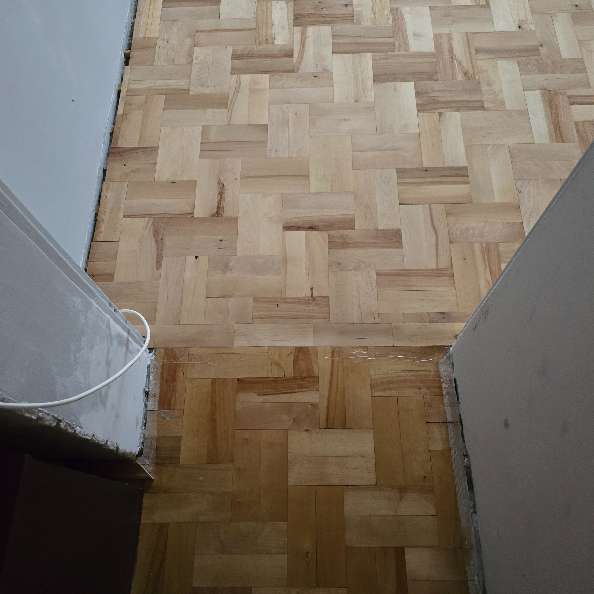 Parkiet ułożony we wzór jodełki francuskiej, widoczne nierówności i szczeliny przy ścianie, ślady kleju montażowego.