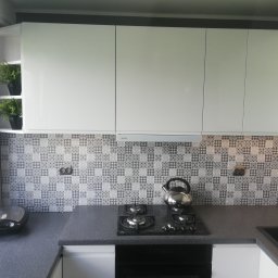 Project ZAZA - Nowoczesna kuchnia w Grudziądzu z białymi szafkami, grafitowym blatem i mozaikową ścianą nad płytą gazową; na blacie czajnik ze stali nierdzewnej i opiekacz.